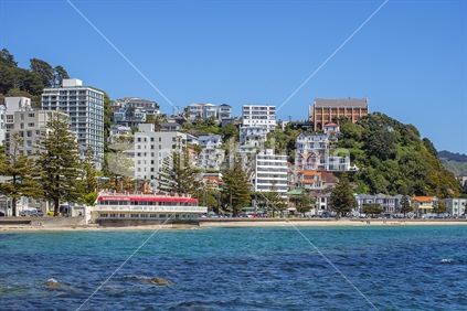 Wellington's Oriental Bay on a fine spring day with blue skies and sea. The iconic rotundah and sandy beach are seen with the expensive apartment blocks lining the bay