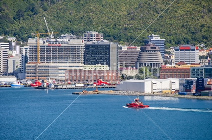 Wellington city and harbour, with a red tugboat creating a wake,