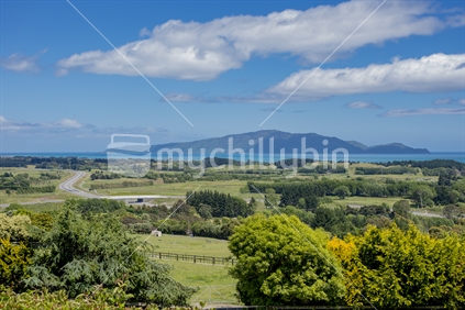 The Kapiti Coast Line as seen from Hadfield Rd near Peka Peka. The Island is seen against a blue sky day. The new expressway can be seen with an overbridge of the old SH1
