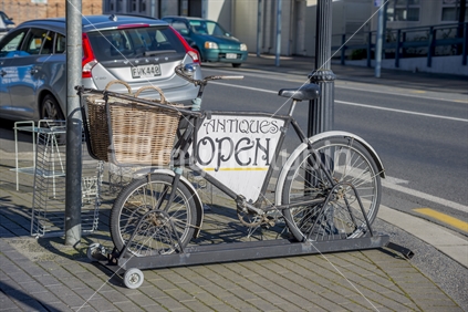 A bicycle displaying an open sign for an antique store in Te Aroha
