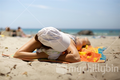 Girl sunbathing on Tawharanui beach in the summertime.