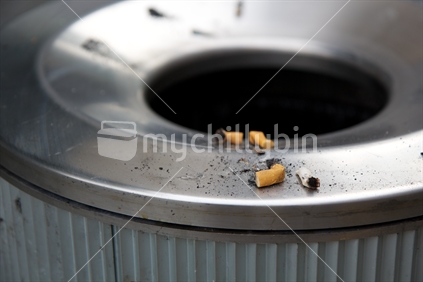 Cigarette butts put out on the rim of a city rubbish bin