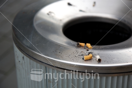 Cigarette butts put out on the rim of a city rubbish bin