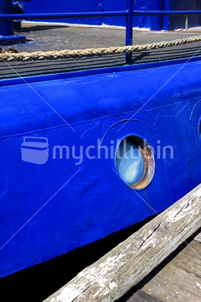 Porthole of an old blue ship tied up to a wharf dock.