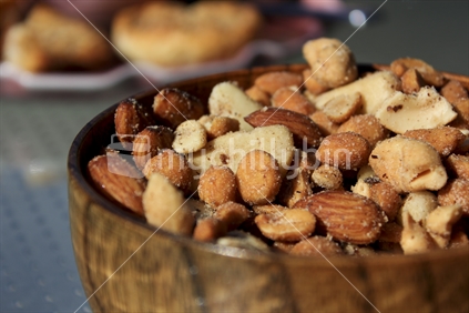 Mixed nuts in a wooden bowl on a table in the sun.