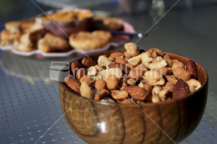 Mixed nuts in a wooden bowl on a table in the sun in New Zealand.