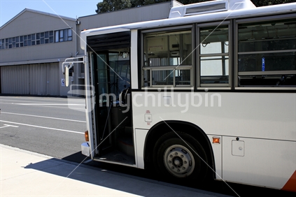 White bus with door open waiting by sidewalk.