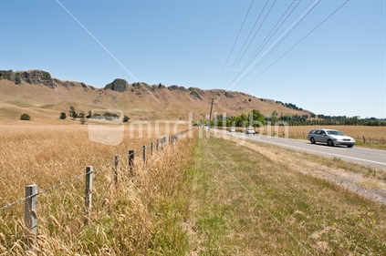 Typical New Zealand Rural Road, with grass, fence, and wires; Waimarama Road near Havelock North, Hawke's Bay with Te Mata Peak in the background.