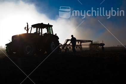 Silhouette of preparations for tractor hayraking -  with surrounding burn off smoke.