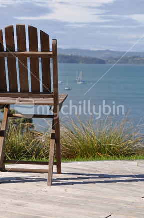 Vacant deck chair on a New Zealand bach deck, overlooking the bay.