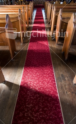 The sun shines onto the pews and aisle in an old country church.