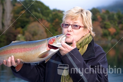 Happy fisherwoman kissing her rainbow trout on Lake Tarawera