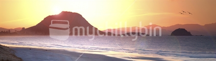 A soft focus stunning panormic shot taken from the sand dunes in Papamoa beach looking back across the sea at Mount Maunganui, Leisure and Rabbit Islands right as the sun retreats behind this landmark for the evening.
