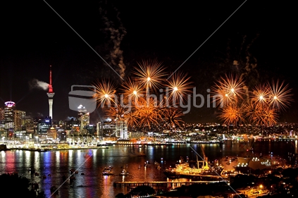 Exploding fireworks at night in Auckland with reflection on the still harbour water, CBD buildings and Naval ships in foreground. Nov 2011.