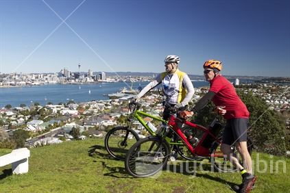 Two bikers rest on top of Mt Victoria with Auckland CBD panorama in background