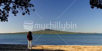 Lone girl looks out across from beach to rangitoto island 
