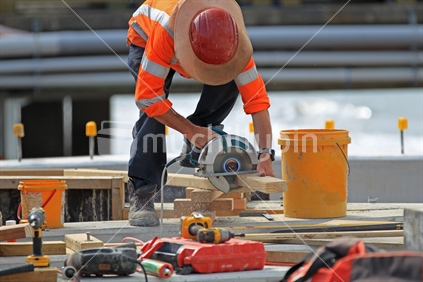 Construction site: builder in safety gear using circular saw