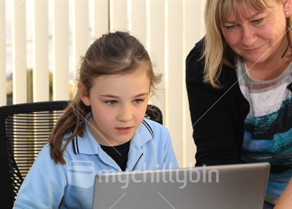 Girl school student working on a computer with teacher or Mum