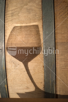Shadow of wine glass on oak barrel in winery cellar