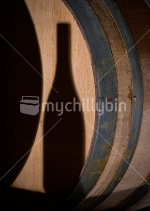 Shadow of wine bottle on oak wine barrel in winery cellar