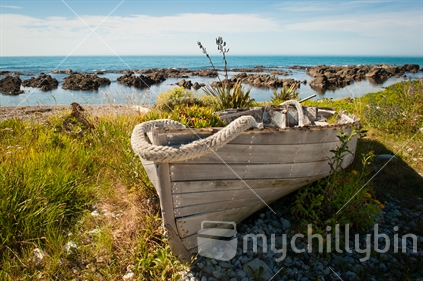 Old wooden fishing boat pulled onto shore to retire, ocean in background.