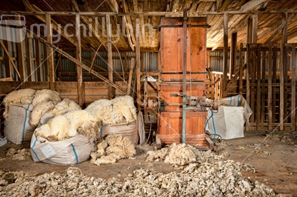 Antique wooden wool press in old shearing shed surrounded by overflowing bales of wool