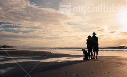 Young couple watching gold sunset from beach with their dog