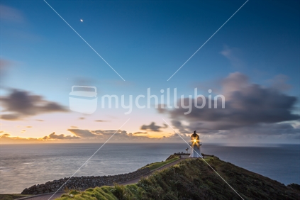 Cape Reinga at blue hour with the moon showing, squalls blowing in the distance. People in distance with motion blur).