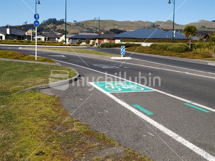 A New Zealand road marked with a lane for cyclists, leading up to a roundabout.