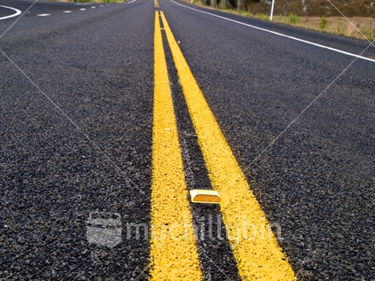 Double yellow lines, and a reflector, on a New Zealand road.