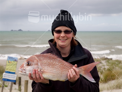 Woman with a snapper freshly caught at Thornton Beach, Bay of Plenty