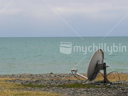A satellite receiver dish on a beach beside a motorhome.
