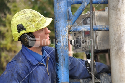 Man in hard hat operating oil drilling rig, Westland, New Zealand.