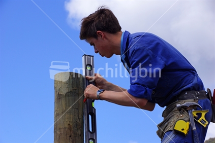 Apprentice builder checking that the fence post is vertical.