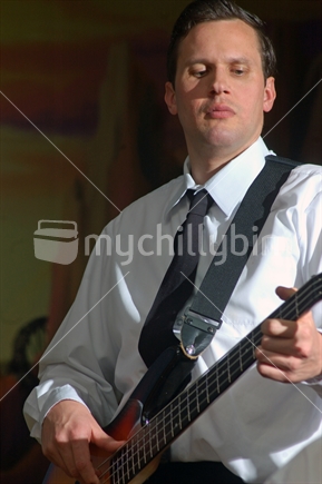 A man playing an electronic bass guitar in a live formal performance.