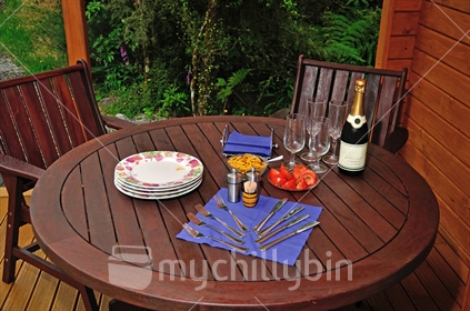 Outdoor table set for an evening barbeque meal on the verandah with tomato and sparking grape juice.