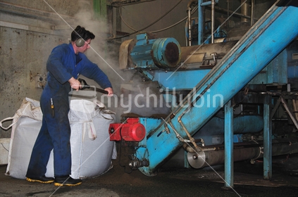 Man shoveling meat meal into an auger at a rendering plant