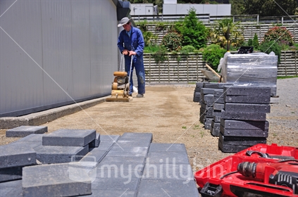 Builder using a vibrating roller before setting out paving stones for a pathway at a construction site in Westland