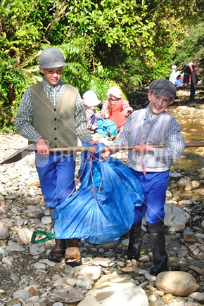 Boys carry their gold mining equipment through Shantytown on an educational field trip