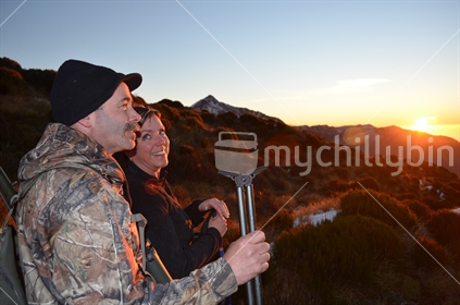 Mature couple enjoy an alpine sunrise in South Westland (lens flare)