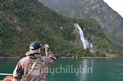 A man filming Bowen Falls at Milford Sound