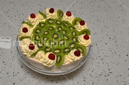 Iconic traditional pavlova, decorated with cream, kiwfruit, and raspberries