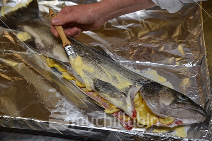 A cook gently bastes a brown trout with butter before it goes in the oven