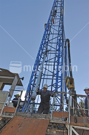 Drilling crewman directs a perforating tool being lowered into an exploratory oilwell on the West Coast.