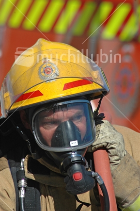 Portrait of fireman wearing breathing apparatus and carrying a fire hose