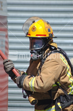 Fireman wearing breathing apparatus pulls a hose from the fire tender