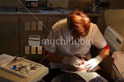 School dental nurse at work on a girl's tooth, curing a filling with UV light. Free dental care is provided for all children in New Zealand. On the West Coast the nurses work in a portable dental surgery.