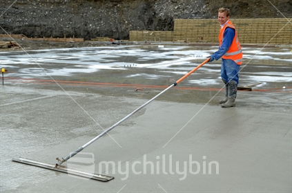 A builder uses a long handled trowel to float off a wet concrete slab for a large building