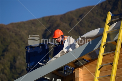 A builder hammers down building paper as the team puts the roof on a large commercial building