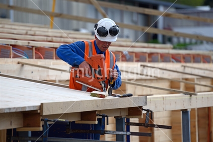 A builder uses a nail gun to secure timber on the verandah of new building